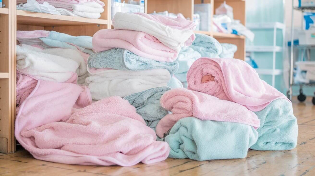 a pile of receiving blankets with a few wrapped around a baby. The blankets are soft, white, and fluffy.