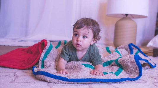 a toddler lying on a weighted blanket and a heating blanket. The toddler is wearing a green shirt and has short brown hair.