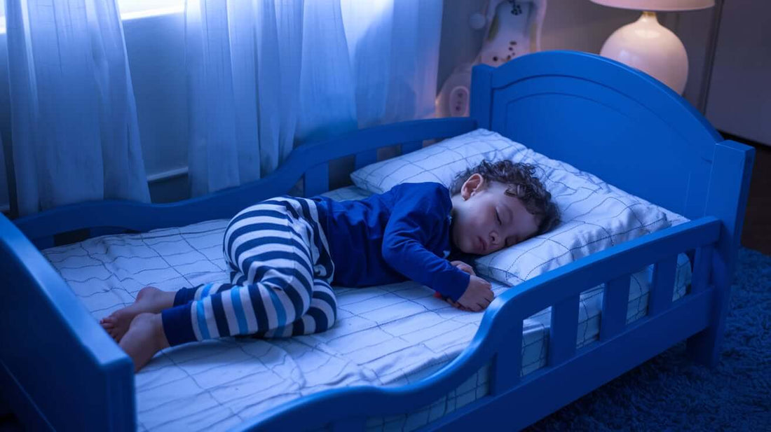 a toddler sleeping on a toddler bed, The toddler is wearing a blue pajama top and a striped pajama bottom.