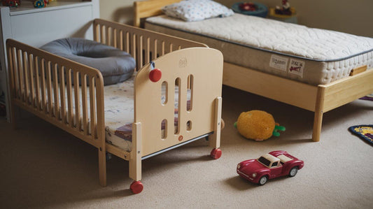 A toddler bed has a rail and a bump-up cushion. A twin bed has a wooden frame and a beige mattress.