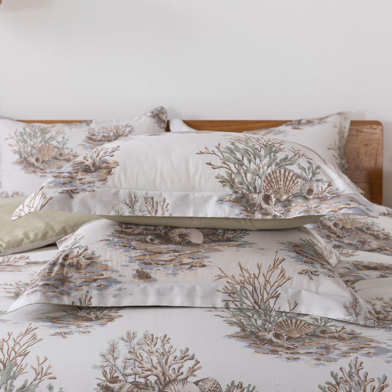 Two green patterned pillows on a bed with candles in the background.