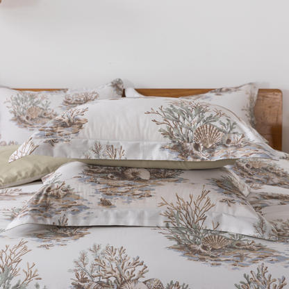Two green patterned pillows on a bed with candles in the background.