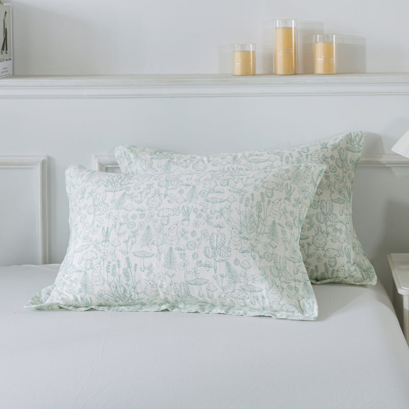 Two green patterned pillows on a bed with candles in the background.