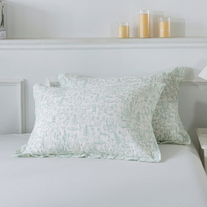 Two green patterned pillows on a bed with candles in the background.